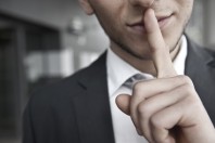 mann mit anzug legt finger auf lippen