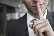 mann mit anzug legt finger auf lippen