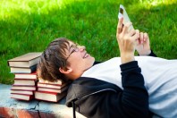 Un adolescent joue à la tablette, adossé à des livres
