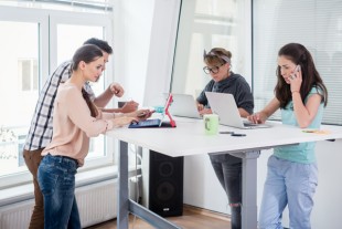 Busy co-workers using mobile technology while sharing a desk in