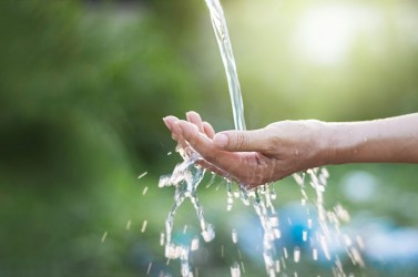 Water pouring in woman hand on nature background, environment issues