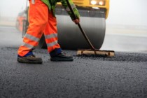 Baustelle: Straßenwalze und Bauarbeiter mit Besen bei der Asphaltfertigung