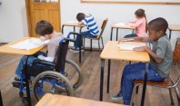 Disabled pupil writing at desk in classroom