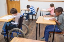 Disabled pupil writing at desk in classroom