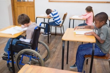 Disabled pupil writing at desk in classroom